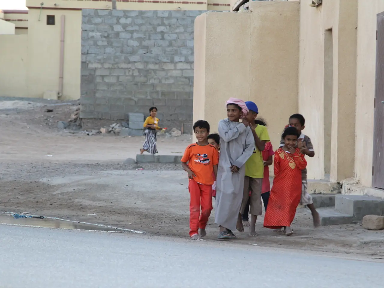 In this image there are group of kids standing and smiling , and there are buildings, water, rocks,...