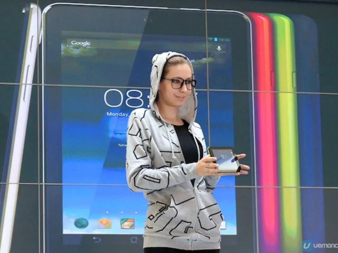 In the image we can see a woman standing, wearing clothes, spectacles and she is smiling, she is...