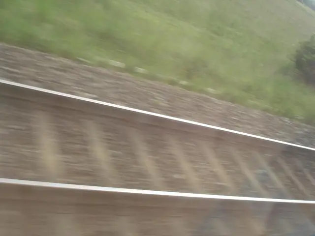 In this image there is a railway track in the middle. There are stones on the track. Beside the...